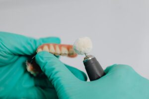 https://www.pexels.com/photo/hands-in-gloves-polishing-teeth-implants-6627600/ a pair of gloved hands polishing a dental bridge