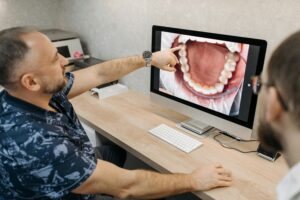 https://www.pexels.com/photo/dentist-sitting-by-desk-and-showing-teeth-on-screen-6812508/ dentist reviewing tooth decay treatment with a patient